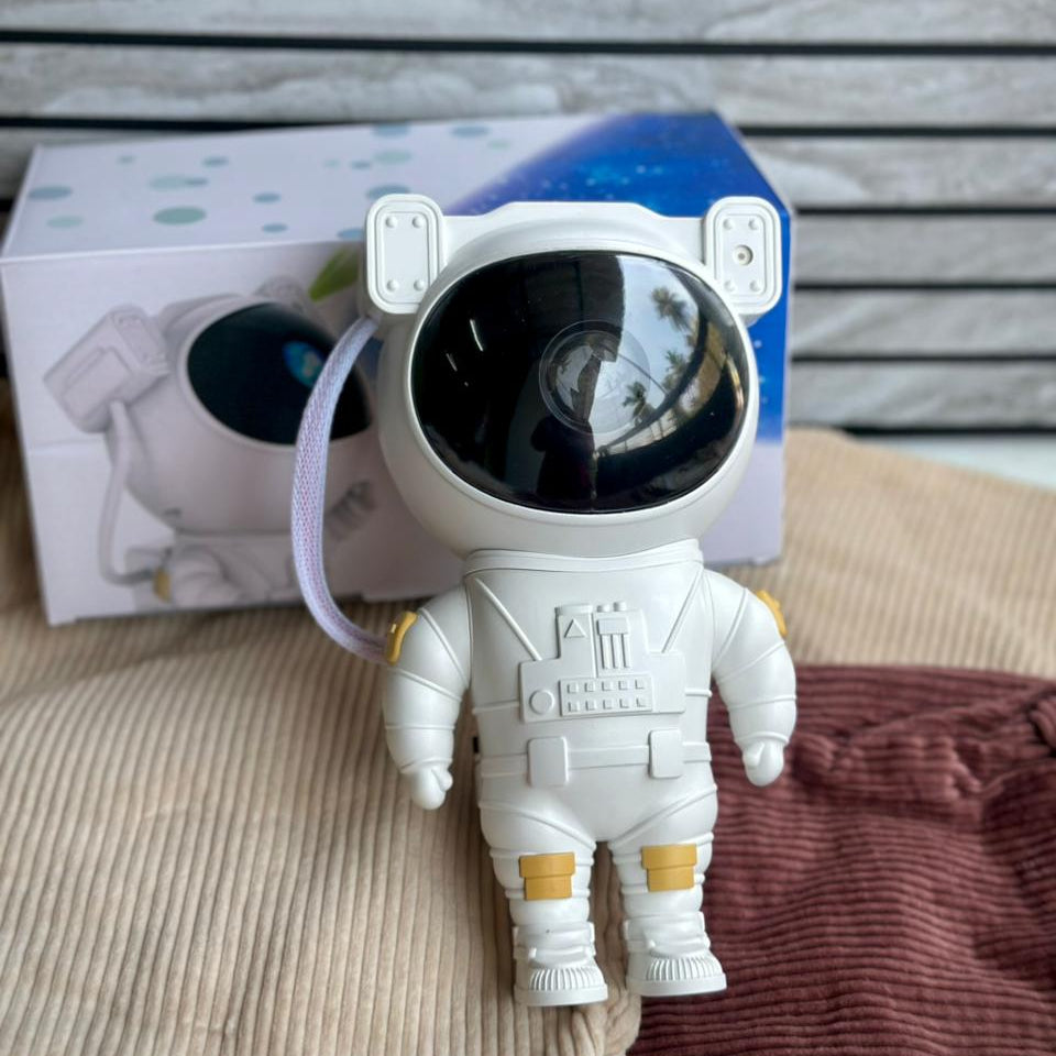 White astronaut toy with a black visor in front of a box on a striped fabric background