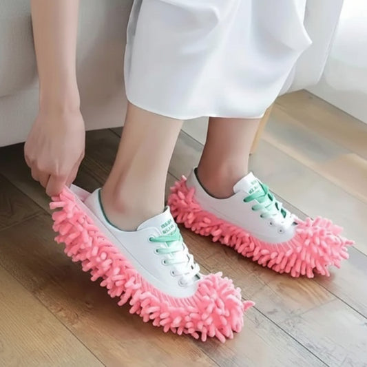Person wearing white sneakers with pink cleaning slippers on a wooden floor.